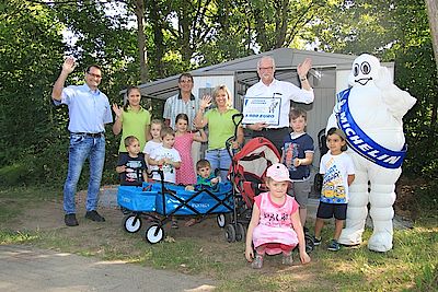 Michelin Personalleiter Peter Kubitscheck übergibt vor der neuen Kinderwagen-Garage einen Symbolscheck an Kita-Leiterin Christa Kossow (hinten, 5. und 4. v. l.). Mit ihr freuen sich (hinten, v. l.) Manuel Herrero (Michelin), Erzieherin Mona Spitzlay, Udo