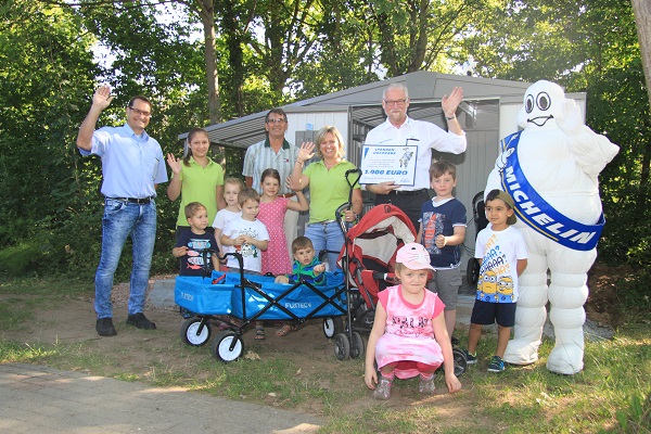 Michelin Personalleiter Peter Kubitscheck übergibt vor der neuen Kinderwagen-Garage einen Symbolscheck an Kita-Leiterin Christa Kossow (hinten, 5. und 4. v. l.). Mit ihr freuen sich (hinten, v. l.) Manuel Herrero (Michelin), Erzieherin Mona Spitzlay, Udo